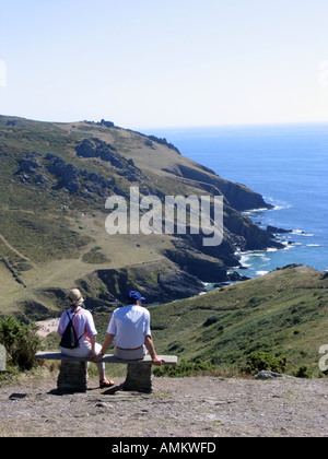 Walkers resting on a bench on a spectacular coastal path overlooking Soar Mill Cove, South Devon, UK Stock Photo