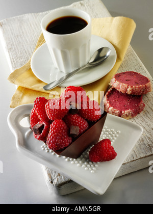Chocolate cake filled with chocolate topped with fresh raspberries in a cafe setting with coffee Stock Photo