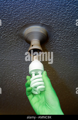 Green hand changing to an energy efficient bulb in ceiling Stock Photo