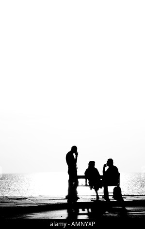 a silhouette with three persons. One is smoking a cigarette. The two others are in conversation in a perfect summer´s day Stock Photo