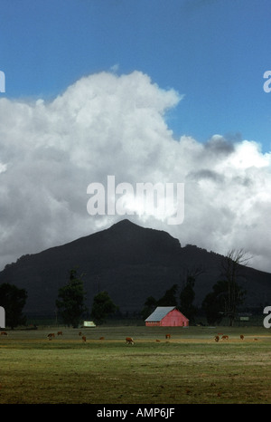 A red barn sits in a valley under a hill in the country Stock Photo