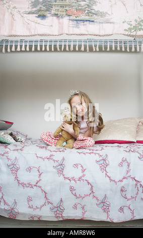 Girl Sitting on Bed, Holding Teddy Bear and Wearing Tiara Stock Photo