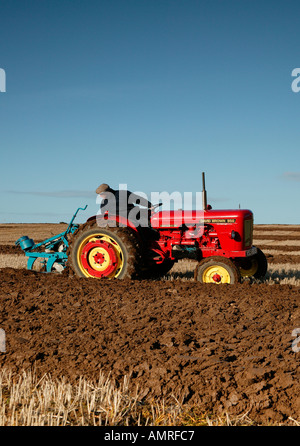 Red Vintage tractor ploughing field with blue sky Stock Photo