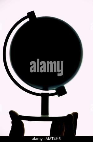 Silhouetted model globe with hand cupping the base Stock Photo