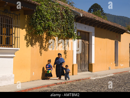 Local woman with two children walking down sunlit cobbled street in Antigua city in the Republic of Guatemala Central America Stock Photo