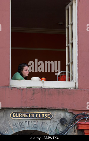 Young woman lost in thought looking out of a window in Burnet s Close Edinburgh Stock Photo