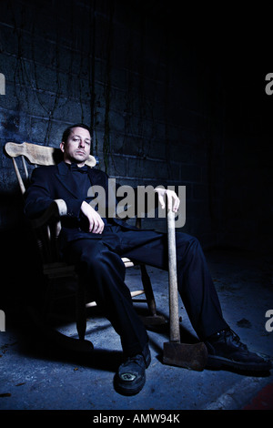 Young adult sitting in a rock chair holding onto an axe Processed to make the image dark and moody Stock Photo