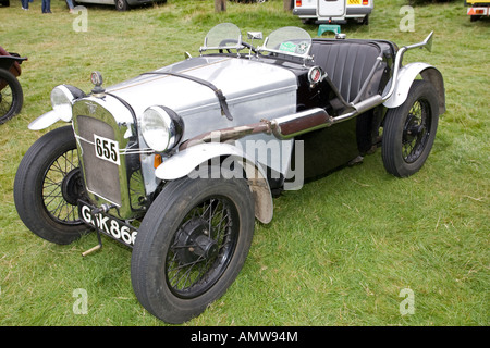 A vintage Austin Seven car parked by racks of tyres in the paddock at