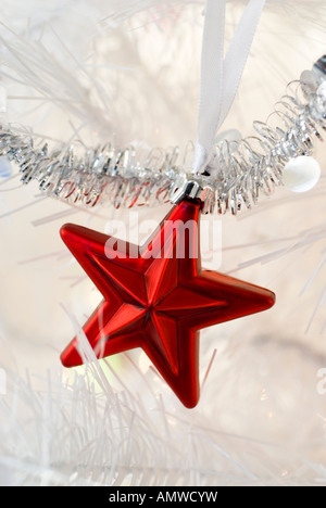A red star holiday ornament hanging on a white artificial Christmas tree. Stock Photo