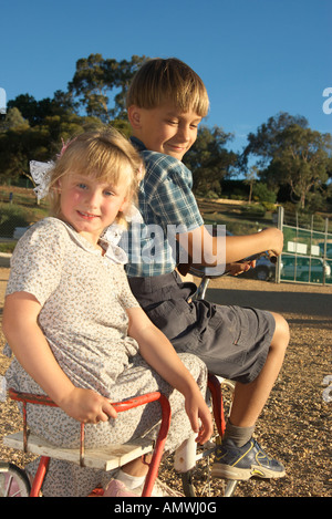 young boy rides off with a girl in the back of the old tricycle Stock Photo