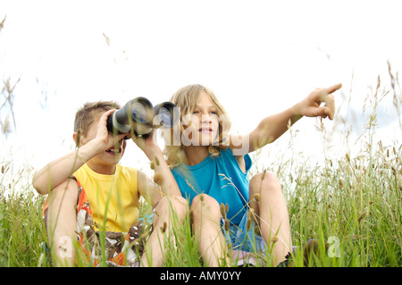 Two boys sitting in grass and using binocular Stock Photo