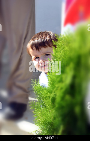 Little girl hiding and peeking behind tree during birthday party Stock Photo