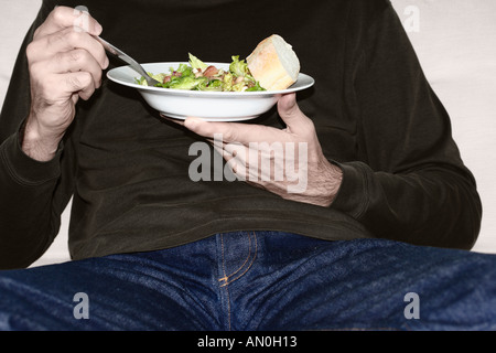 Man On Sofa Eating Bowl Of Salad Stock Photo