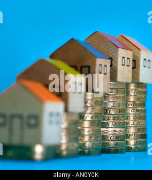 piles of pound coins with toy houses on top showing rise and falls in the property market, interest rates and mortgages Stock Photo