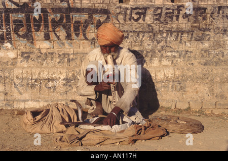 Snake charmer playing pipes and crouching against a wall India Stock Photo