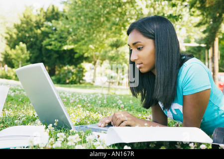 Indian female college student working on laptop in grass Stock Photo