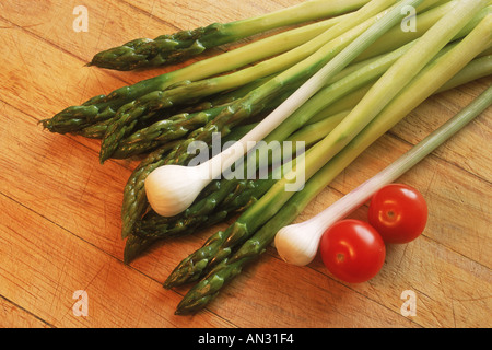 Asparagus with green onions and tomatoes on wooden cutting board Stock Photo