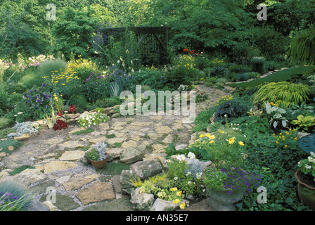 Peaceful: A flagstone path and patio in a private backyard flower garden leads through a wood arbor with seat Missouri USA Stock Photo