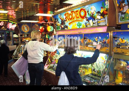 Girls playing on the penny slot machines in an amusement arcade, England UK Stock Photo