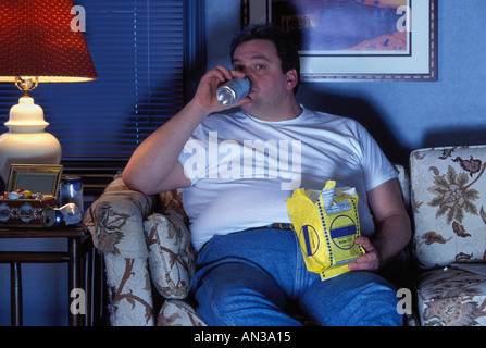 Overweight Couch potato man watching TV drinking beer and eating popcorn Stock Photo