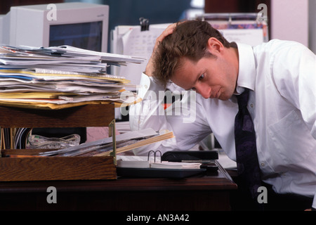 Stressed male office worker sitting at desk with piles of Paperwork Stock Photo