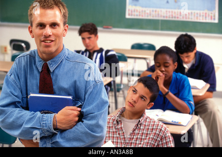 Portrait of high school teacher in classroom with students working at desks Stock Photo