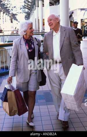 Caucasian senior couple shopping walking talking laughing with shopping bags in mall Stock Photo