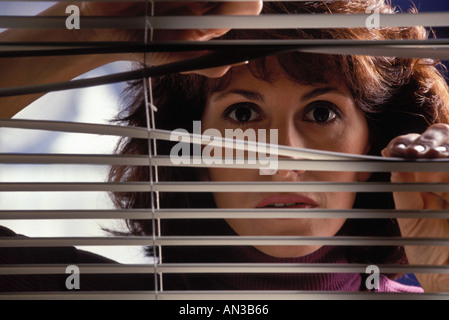 Caucasian woman parting venetian blinds looking apprehensive, fearful, and concerned for her safety Stock Photo