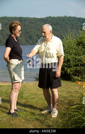 seniors man and woman having discussions on the beach beside a blue lake Stock Photo