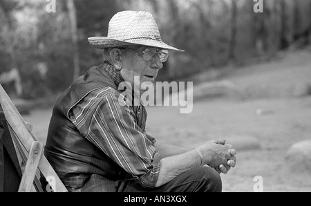 Old man sitting in deck chair on the beach wearing a straw hat. Stock Photo