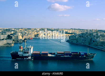 Large cargo ship sails into Valletta harbour / port, Malta - with a pilot boat / tug in the afternoon light Stock Photo