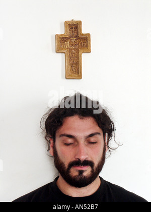 Man's head under cross hanging on the wall eyes shut praying Stock Photo