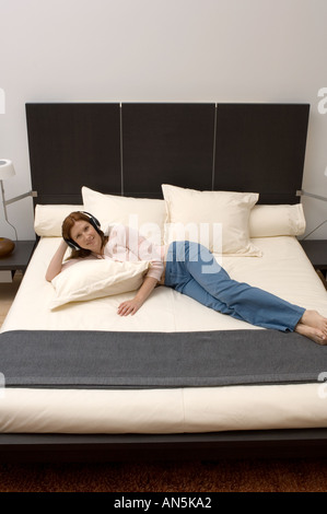 Portrait of woman listening to music on her headphones while laying in bed Stock Photo