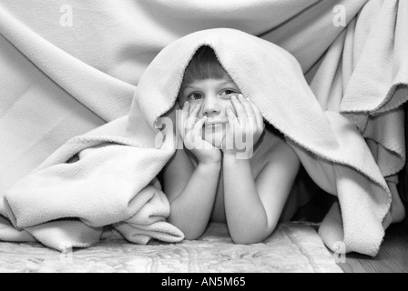 Small boy smiling hiding under blanket Stock Photo