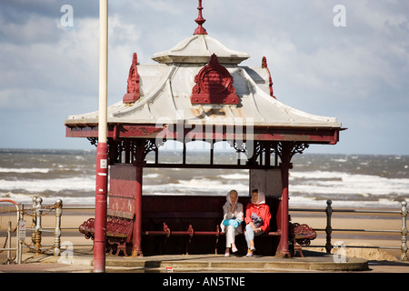 Two elderly women sit in a faded Victorian shelter on the promenade at Blackpool UK on August bank holiday Stock Photo