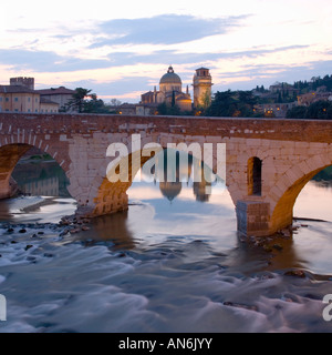 Verona, Veneto, Italy. The Ponte Pietra over the River Adige illuminated at dusk, the Chiesa di San Giorgio in Braida beyond. Stock Photo