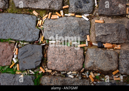 CIGARETTE STUBS BETWEEN COBBLE STONES IN AN URBAN LOCATION UK Stock Photo