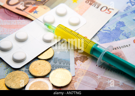 medical syringe filled with yellow liquid and white strip of pills lying on Euro bills and coins Stock Photo