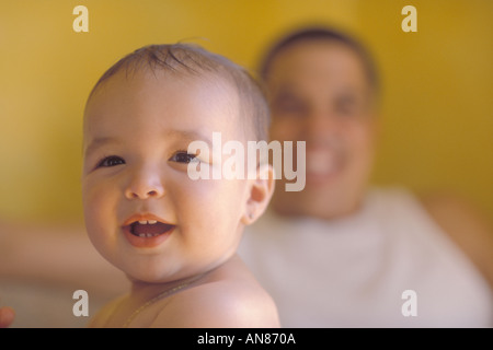 15 month mixed Hispanic girl in foreground with 39 year old Hispanic father in background Stock Photo