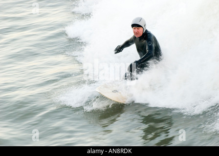 A colour landscape image of a middle aged surfer riding a wave in the seaside resort of Bournemouth,Dorset,England. Stock Photo