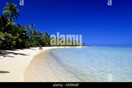 People walking on a picture postcard beach in remote Aitutaki atoll Cook Islands palm trees lined beach. Stock Photo