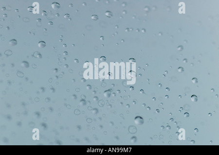 Horizontal abstract close up of rain drops on a pane of glass on a grey day. Stock Photo