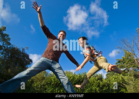 Horizontal portriat of young caucasian adults in mid air against a blue sky, bouncing on a trampoline. Stock Photo