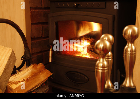 Out of focus fire irons and log basket in front of a blazing cast iron log burner fire Stock Photo