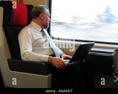 Businessman with laptop computer seated in train cabin looking through the window Stock Photo