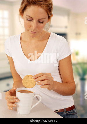 WOMAN IN KITCHEN DUNKING BISCUIT INTO MUG OF TEA Stock Photo