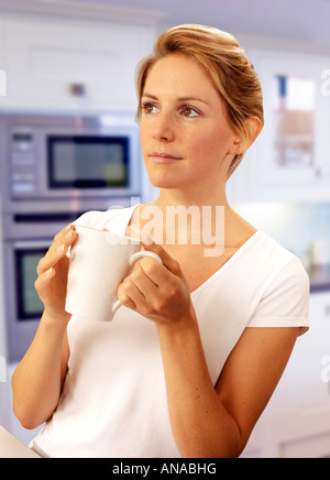 WOMAN IN KITCHEN HOLDING MUG OF COFFEE / TEA Stock Photo