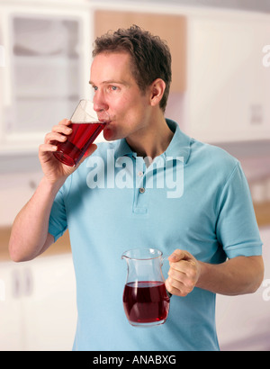 MAN IN KITCHEN DRINKING POMEGRANATE JUICE Stock Photo