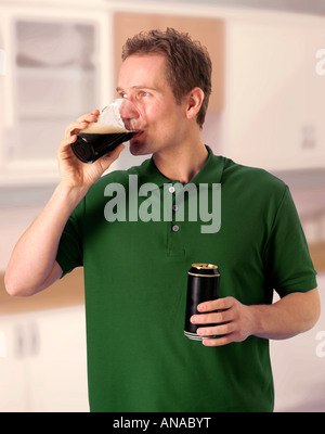 MAN IN KITCHEN DRINKING GUINNESS OR DRY STOUT ALE Stock Photo