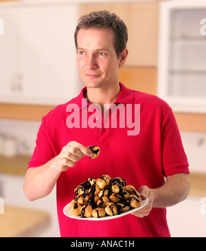 MAN IN KITCHEN HOLDING PLATE OF PROFITEROLES Stock Photo